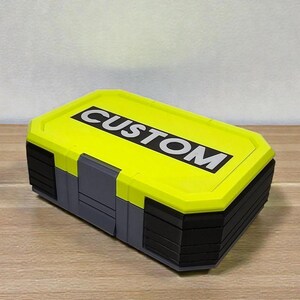 May include: A rectangular storage container with a bright yellow lid and gray body. The lid features the word "CUSTOM" in bold white letters. The container has a black base and is sitting on a wooden surface.