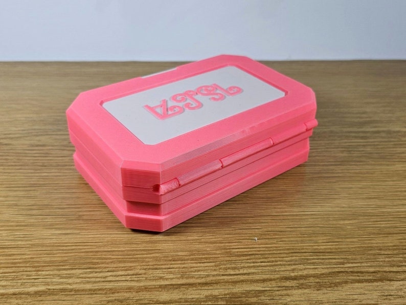 May include: A pink, rectangular box with a white lid. The lid has the word "Lego" embossed on it.