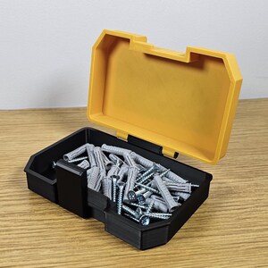 May include: A yellow and black plastic storage box with a lid open, revealing a collection of gray plastic wall anchors.