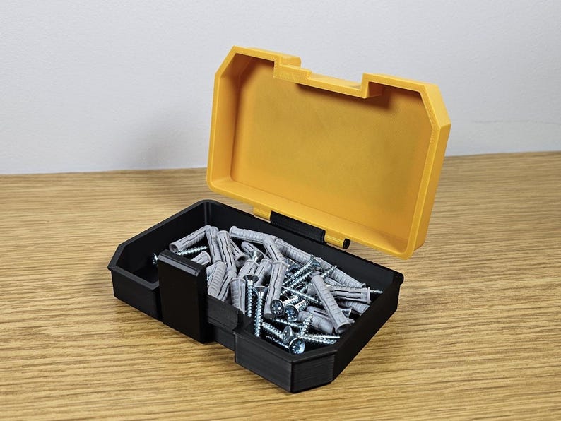 May include: A yellow and black plastic storage box with a lid open, revealing a collection of gray plastic wall anchors.