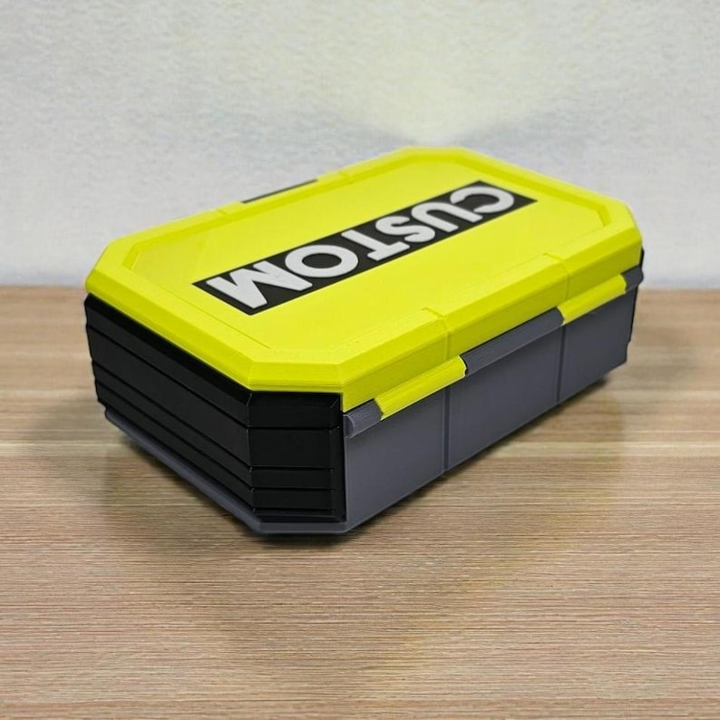 May include: A rectangular storage box with a bright yellow lid and gray base. The lid features the word "CUSTOM" in bold white letters. The box has a multi-tiered design and is suitable for organizing small items.