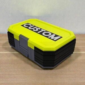 May include: A rectangular storage container with a bright yellow lid and black and gray body. The lid features the word "CUSTOM" in bold white letters. The container is sitting on a wooden surface.