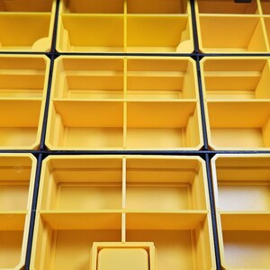 May include: Close-up of a modular storage organizer with multiple yellow compartments. The compartments are divided into sections by vertical and horizontal dividers, with black borders. The organizer is designed for small parts storage.