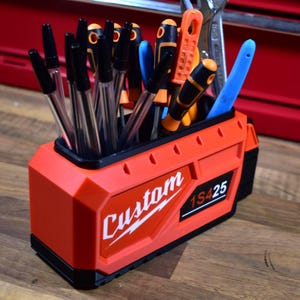 Könnte beinhalten: Ein rot-schwarzer Werkzeugorganizer mit dem Wort "Custom" in weißer Schrift. Der Organizer ist mit Stiften, Schraubendrehern und anderen Werkzeugen gefüllt. Der Text "1S425" ist ebenfalls auf der Seite zu sehen.