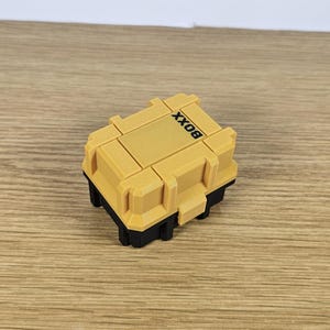 May include: A small yellow plastic box with black trim and the word "BOX" printed on the top.
