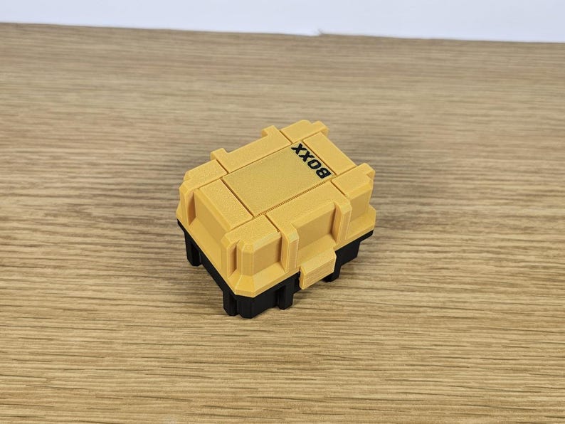 May include: A small yellow plastic box with black trim and the word "BOX" printed on the top.