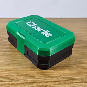 May include: A green and black plastic storage box with the word "Charlie" printed on the top.
