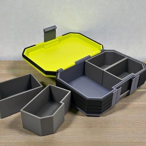 May include: A gray and black storage box with a bright yellow interior and a hinged lid. The box has multiple compartments and is accompanied by several smaller gray containers. The design is modern and geometric.