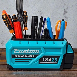 May include: A teal desk organizer with the word "Custom" and "DESK ORGANISER" printed on the front. The organizer holds various tools, including screwdrivers, pens, and scissors. The text "1S425" is also visible.