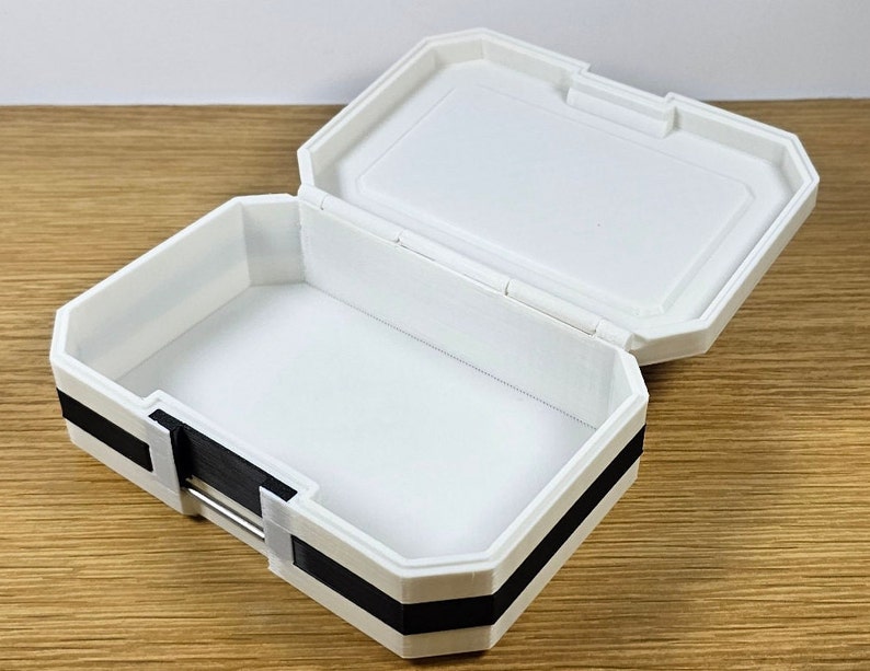 Puede incluir: Una caja de pl&aacute;stico blanca con un borde negro. La caja est&aacute; abierta y el interior est&aacute; vac&iacute;o.