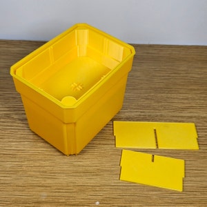 May include: A yellow plastic storage box with a lid and three separate compartments. The box is open and the lid is off.