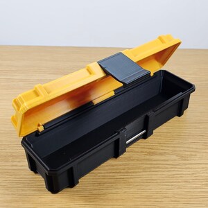 May include: A small, yellow and black plastic toolbox with a hinged lid. The lid is open and the inside of the box is empty.