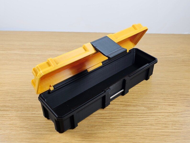 May include: A small, yellow and black plastic toolbox with a hinged lid. The lid is open and the inside of the box is empty.