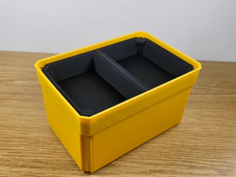 May include: A yellow plastic storage box with two compartments. The compartments are lined with black plastic.