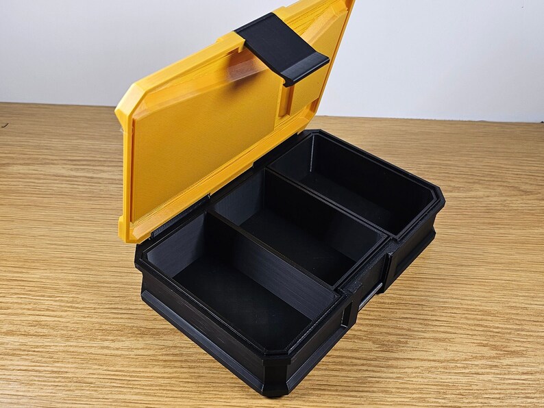 May include: A yellow plastic storage box with a black lid and three compartments. The lid is open and the compartments are empty.