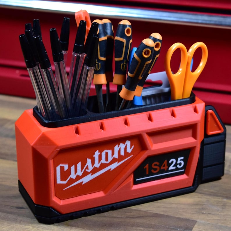 May include: An orange and black tool organizer with the word "Custom" and "1S425" printed on the side. The organizer holds pens, screwdrivers, and scissors. The organizer is made of plastic.
