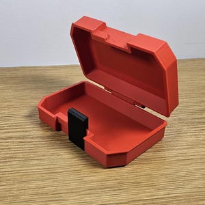 Op de afbeelding: Een rode plastic opbergdoos met een zwart slot. De doos is open en leeg.
