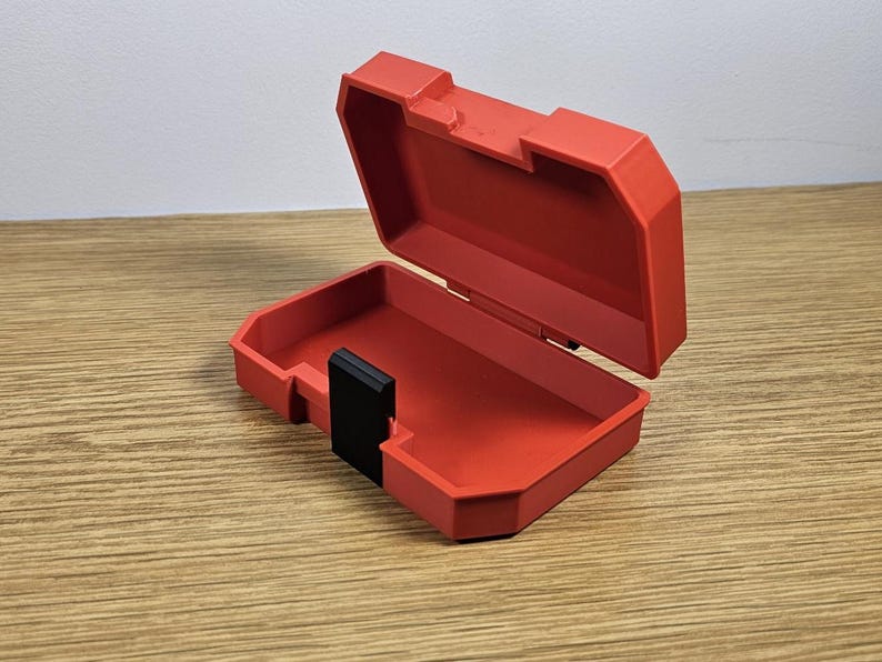 Op de afbeelding: Een rode plastic opbergdoos met een zwart slot. De doos is open en leeg.