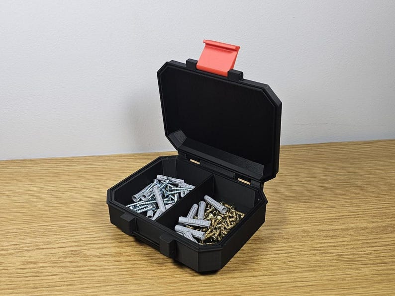 May include: A black, open toolbox with a red latch, filled with screws and wall anchors. The toolbox is divided into three compartments, each containing different types of hardware. The toolbox is sitting on a wooden surface.