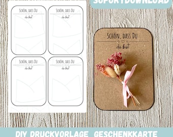 May include: Printable gift card template with the text "SCHÖN, DASS DU DA BIST" (German for "It's nice that you are here") and a simple design of a heart and a banner. The template is shown on a wooden background with a small bouquet of dried flowers.