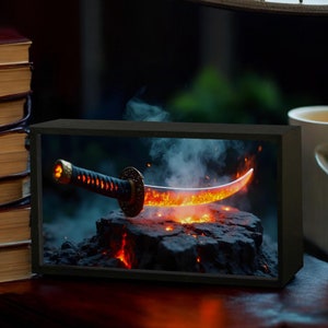 Op de afbeelding: Een zwart katana-zwaard met een gouden handvat ligt op een bed van gloeiende kolen. Het zwaard is omgeven door rook en vonken.