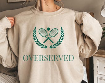 May include: A beige sweatshirt with a green tennis racket and ball graphic and the text "OVERSERVED".