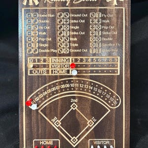 Könnte beinhalten: Baseball-Scorekeeper aus Holz mit dem Text "Ranley Scout" und Teamlogos. Verfügt über ein Baseballfeld-Diagramm, einen Inning-Tracker und Würfel. Enthält rote und weiße Marker zum Verfolgen von Runs und Outs.