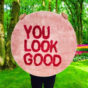 Puede incluir: Una alfombra redonda rosa con las palabras "YOU LOOK GOOD" en letras rojas.