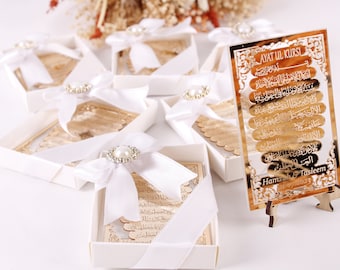 Puede incluir: Cajas decorativas doradas con cinta de satén blanca y detalles de perlas, que contienen un marcapáginas dorado con caligrafía árabe y el texto "Ayat ul Kursi" y "Hamzah & Tasleem 11/11/2023".