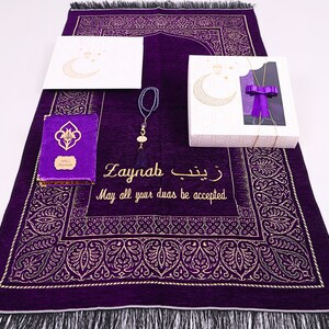 May include: A purple prayer rug with gold embroidery and a personalised inscription that reads "Zaynab May all your duas be accepted". The rug is part of a gift set that includes a prayer book, a set of prayer beads, and a gift box with a crescent moon design.