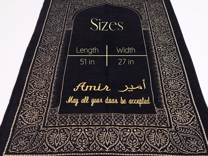May include: Black prayer rug with gold embroidery featuring a traditional Islamic design. The rug measures 51 inches long and 27 inches wide. It has the name "Amir" and the Arabic phrase "أمير" written in gold. The text "May all your duas be accepted" is also written in gold.