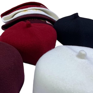 Puede incluir: Cinco sombreros de fieltro en diferentes colores, incluyendo burdeos, rojo, blanco y negro. Los sombreros son todos redondos y tienen una pequeña protuberancia en la parte superior.