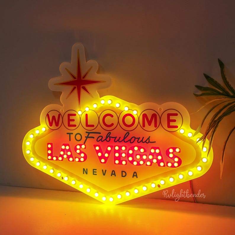 May include: A yellow and red neon sign with white bulbs that reads "Welcome to Fabulous Las Vegas Nevada".
