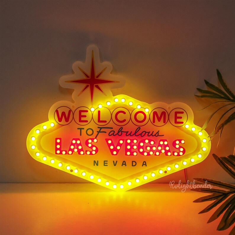 May include: A yellow and red neon sign with white bulbs that reads "Welcome to Fabulous Las Vegas Nevada".