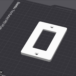 Op de afbeelding: Een witte, rechthoekige lichtschakelaar cover met een rechthoekige opening in het midden en twee schroefgaten. Het ligt op een donkergrijze ondergrond. De tekst "Bambu Textured PE Plate" is zichtbaar.