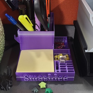 May include: A purple 3D-printed desk organizer with compartments for pens, scissors, and sticky notes. The organizer has the name "Smashlee" printed on the front. Includes a small blue TARDIS model and star-shaped decorations.