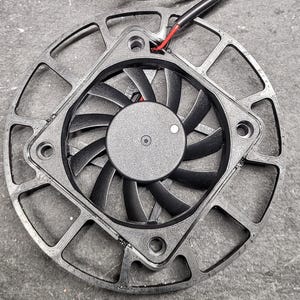 May include: Two black computer fans with curved blades and a central hub. Each fan has a square frame with a circular fan inside. Wires with red and black insulation extend from the fans.