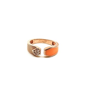 May include: A gold ring with a textured band and a bright orange enamel inlay. The ring has a small cluster of clear stones on one side.