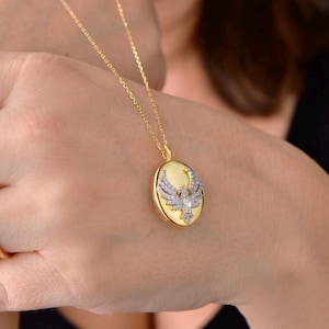 May include: A gold chain necklace with a round pendant featuring a detailed eagle design with clear sparkling stones.