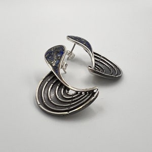 Op de afbeelding: Een paar zilveren oorbellen met een blauwe lapis lazuli-steen inlay. De oorbellen zijn gevormd als een halve maan met een gelaagd ontwerp.