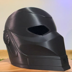 May include: A black plastic helmet with a visor and a textured surface. The helmet has a small, round detail on the side.