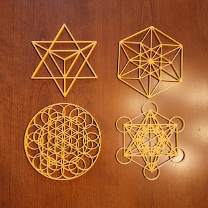 Op de afbeelding: Set van vijf goudkleurige geometrische vormen, waaronder een davidster, een levensbloem, een kubus en twee andere geometrische vormen.