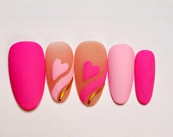 May include: Set of six pink and peach false nails with a heart and wavy line design. The nails are oval shaped and have a matte finish.