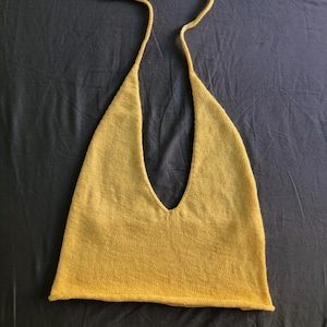 May include: Mustard yellow halter top with a deep V-neck. The top is knitted and has long, thin straps that tie behind the neck. The garment is laid flat on a dark grey surface.