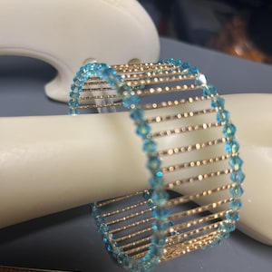 May include: A gold wire bracelet with turquoise blue crystal beads. The bracelet is about 3 inches in diameter.