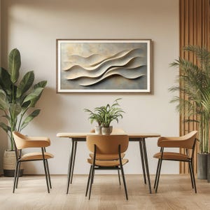 May include: A rectangular wall art piece featuring layered, cream-colored abstract waves with soft shadows, framed in wood. The artwork is displayed above a wooden dining table with three tan chairs and two potted green plants on either side.