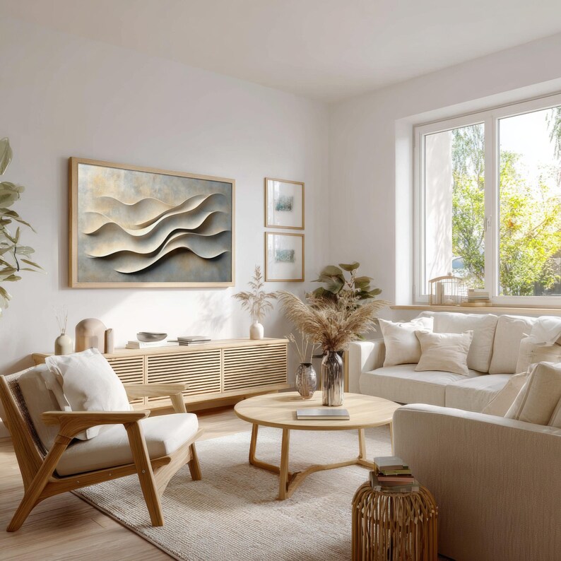 May include: A rectangular wall art piece featuring abstract, layered, cream-colored wave shapes on a textured background, framed in light wood. The artwork is displayed above a long, slatted wooden media console in a bright, neutral-toned living room.