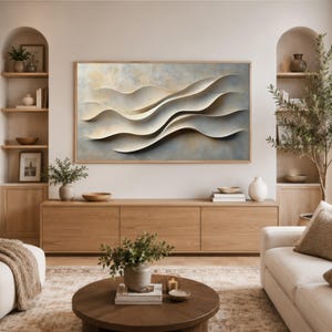 May include: A rectangular wall art piece featuring abstract, layered, cream-colored wave shapes against a textured, muted blue and gold background, framed in light wood, displayed above a long wooden media console in a living room.