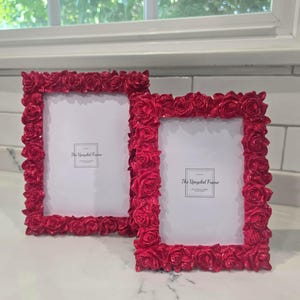 May include: Two rectangular picture frames with vibrant red rose detailing. The frames have a glossy finish and feature the text "The Upcycled Frame". The frames are empty, ready for photos.