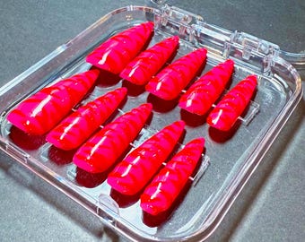 May include: A set of ten bright red, pointed artificial nails with a vibrant pink swirl design, neatly arranged in a clear plastic case. The nails are glossy and appear ready for application, showcasing a bold and eye-catching aesthetic.